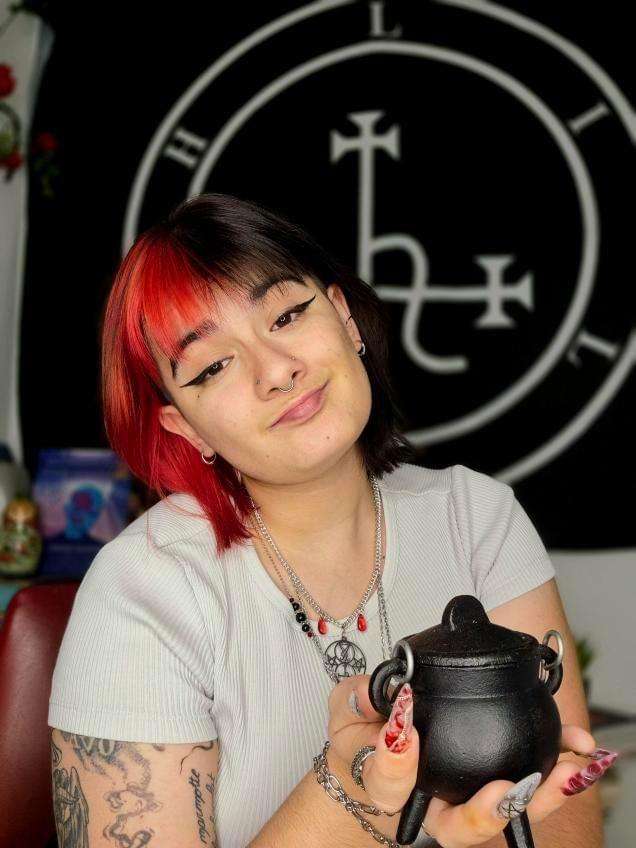 Hele, la coiffeuse du Coven de Hele, arbore une coloration split hair rouge et noir, un contraste audacieux et mystique reflétant son univers ésotérique.